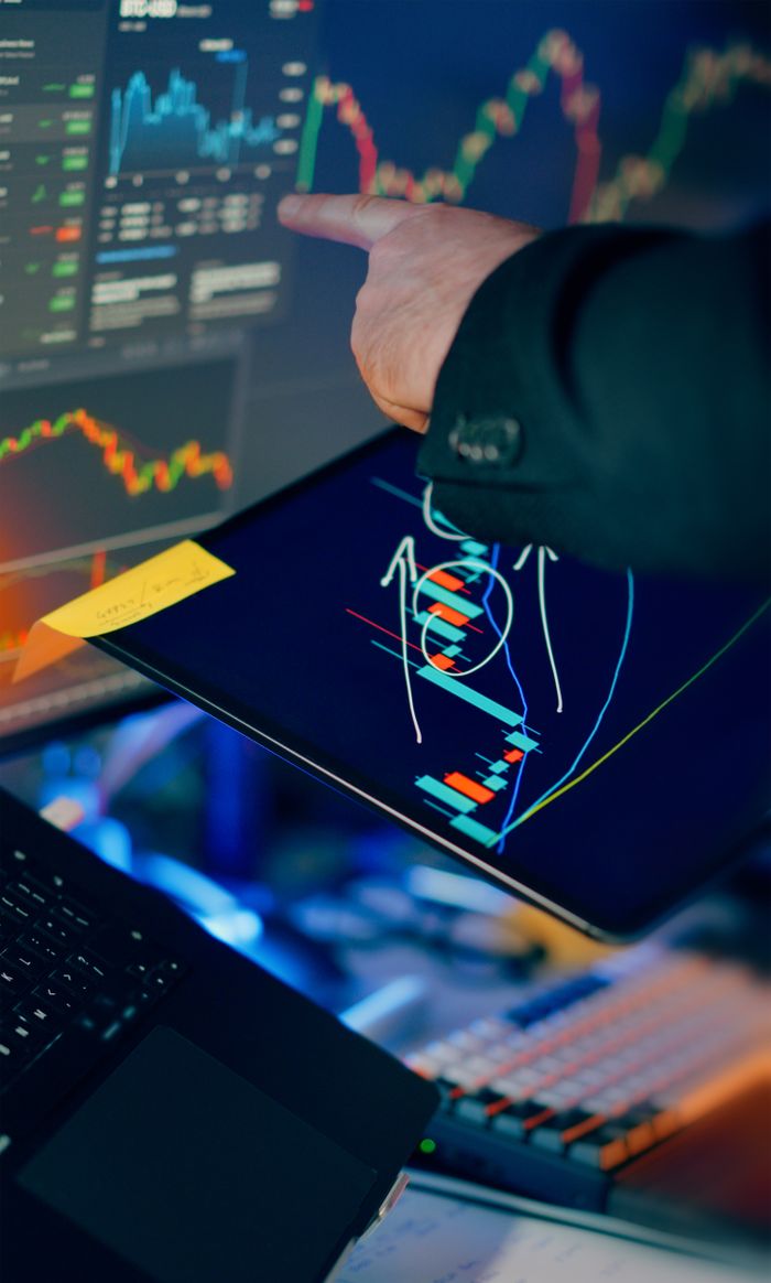 services-01 A business professional examines financial charts on a tablet and monitor for investment strategy.