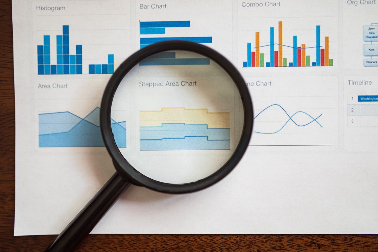 services-03 A magnifying glass focuses on various business charts and graphs on paper.